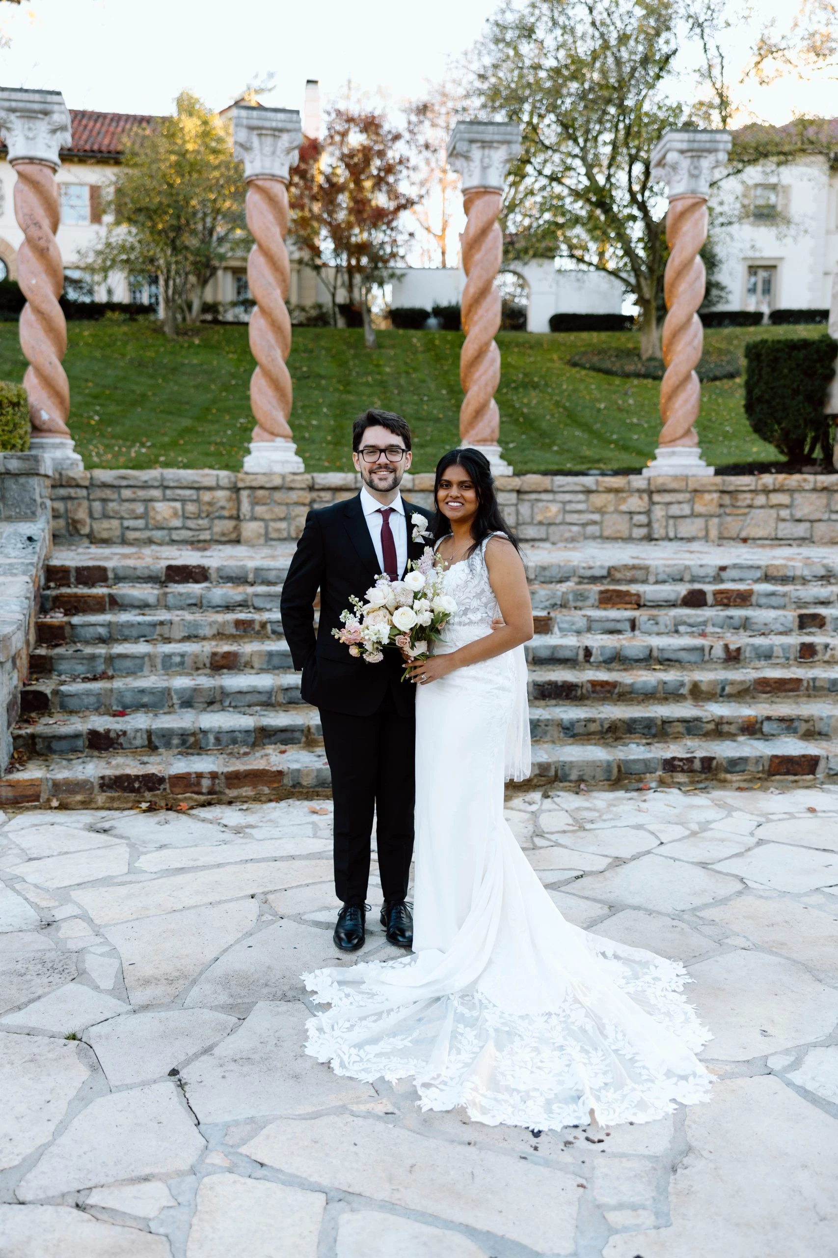 true bride sereena posing next to husband william in from of stone pillars and brick steps - 7715 by Stella York