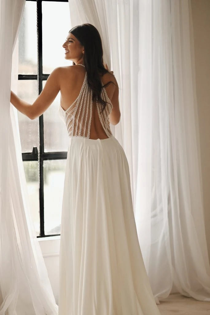 Bride looking out the window wearing a wedding dress with draping pearls along her back