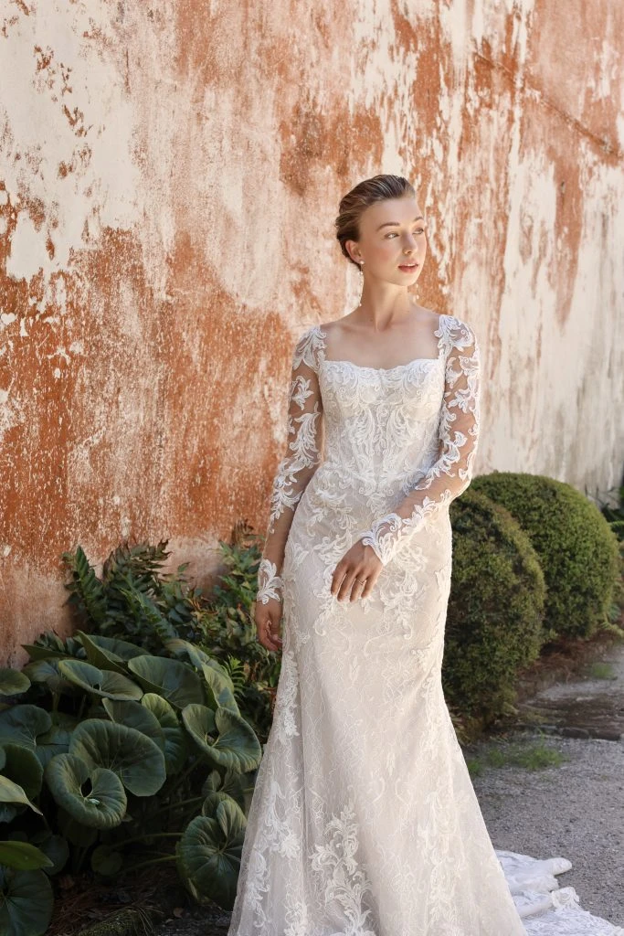 bride standing outside next to a building wearing a floral lace wedding gown.