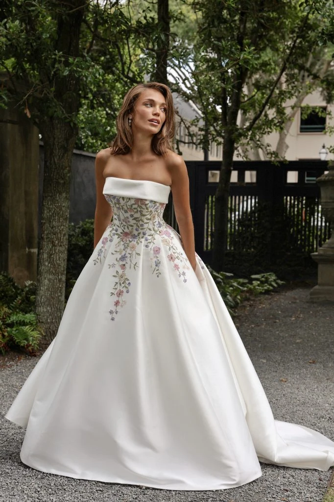 Bride with hands in her pockets wearing a strapless ballgown with embroidered flowers