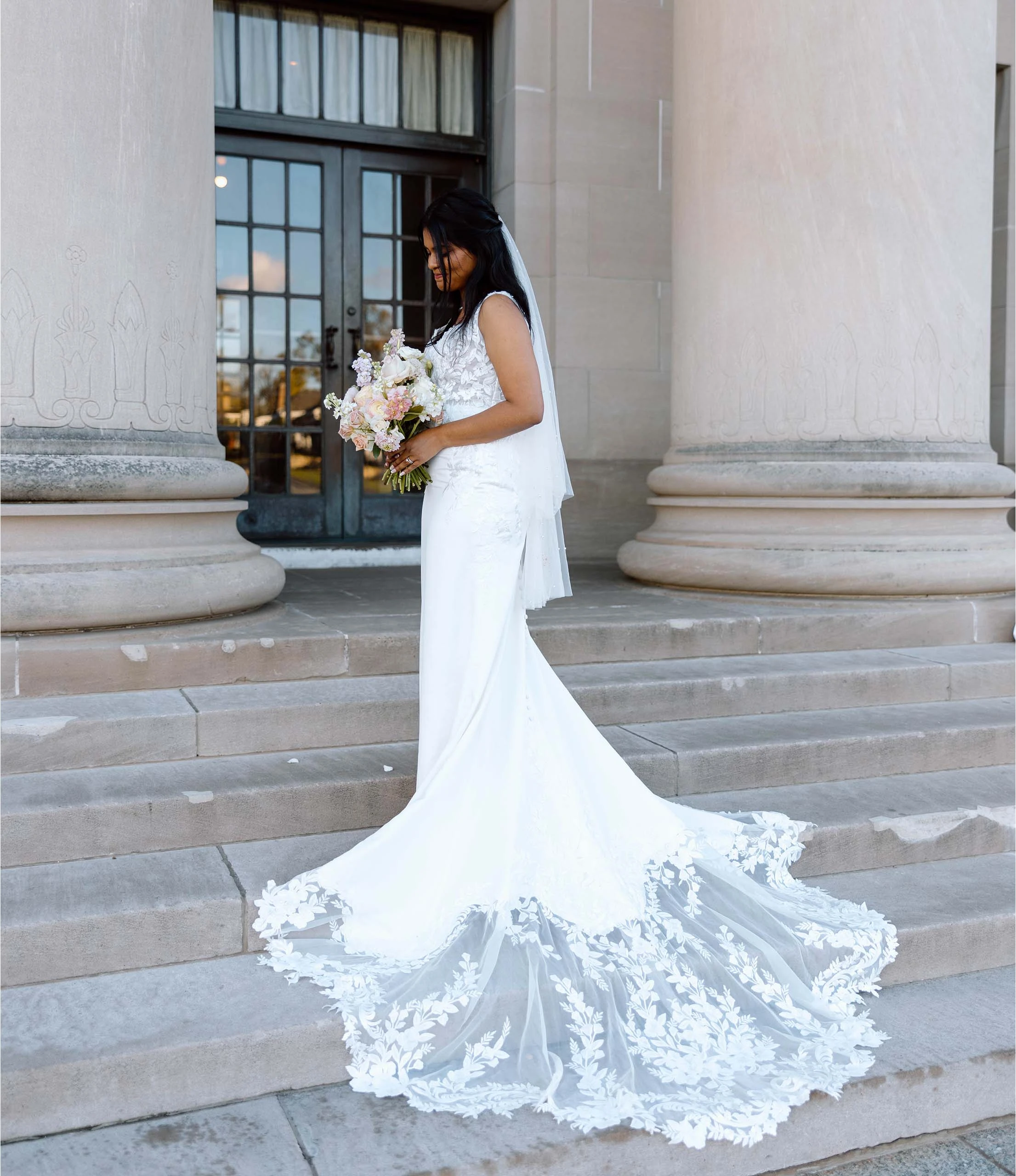 true bride sereena posing on stone steps in 7715 by Stella York and holding bouquet.