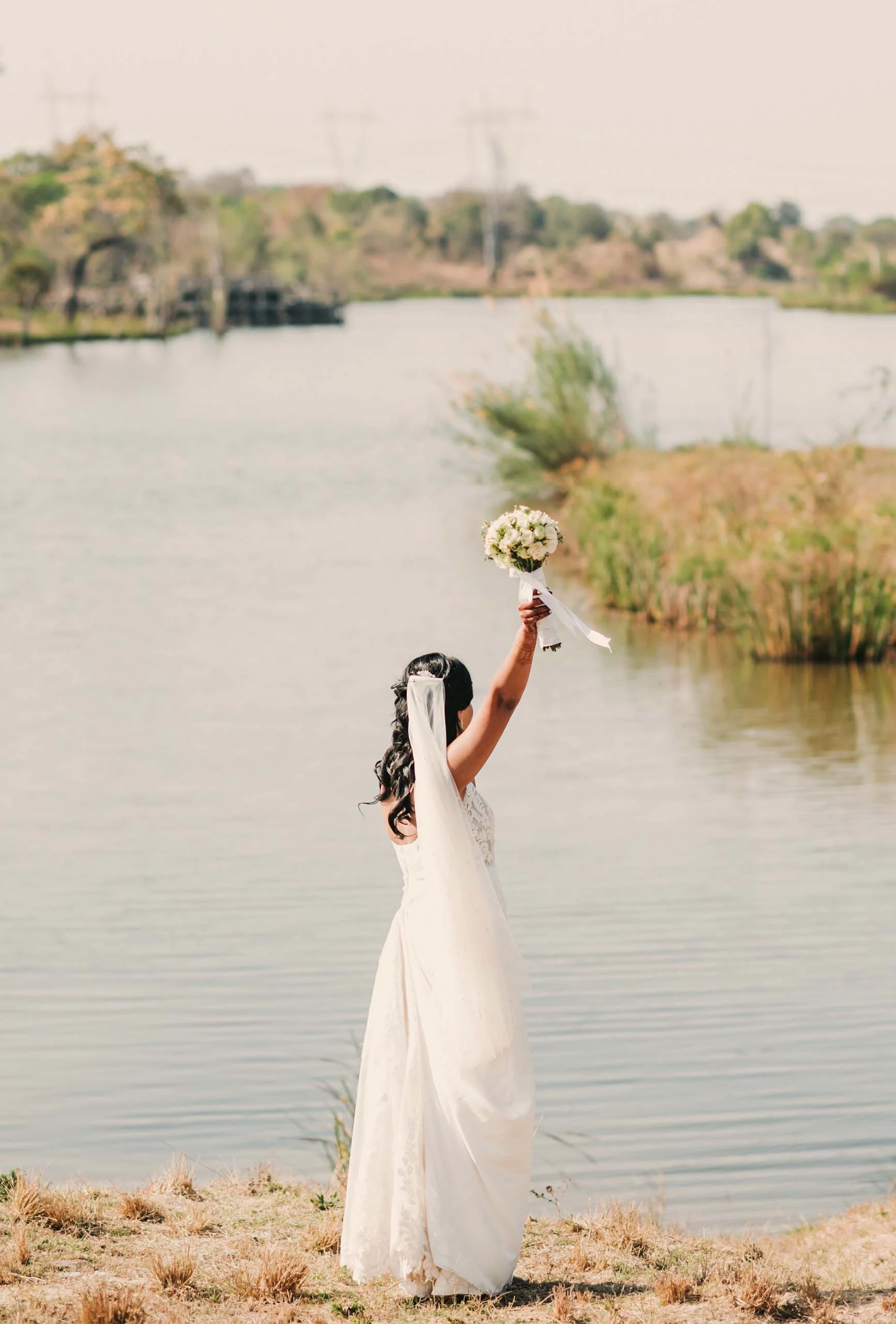 true bride sereena holding bouquet up in the air while looking out over a lake - 7715 by Stella York