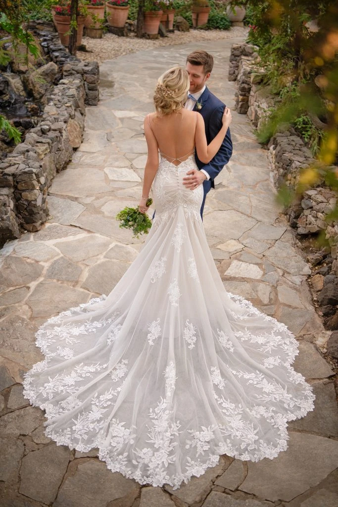 Bride and groom embracing in a garden with the bride wearing a lace fit-and-flare wedding dress.