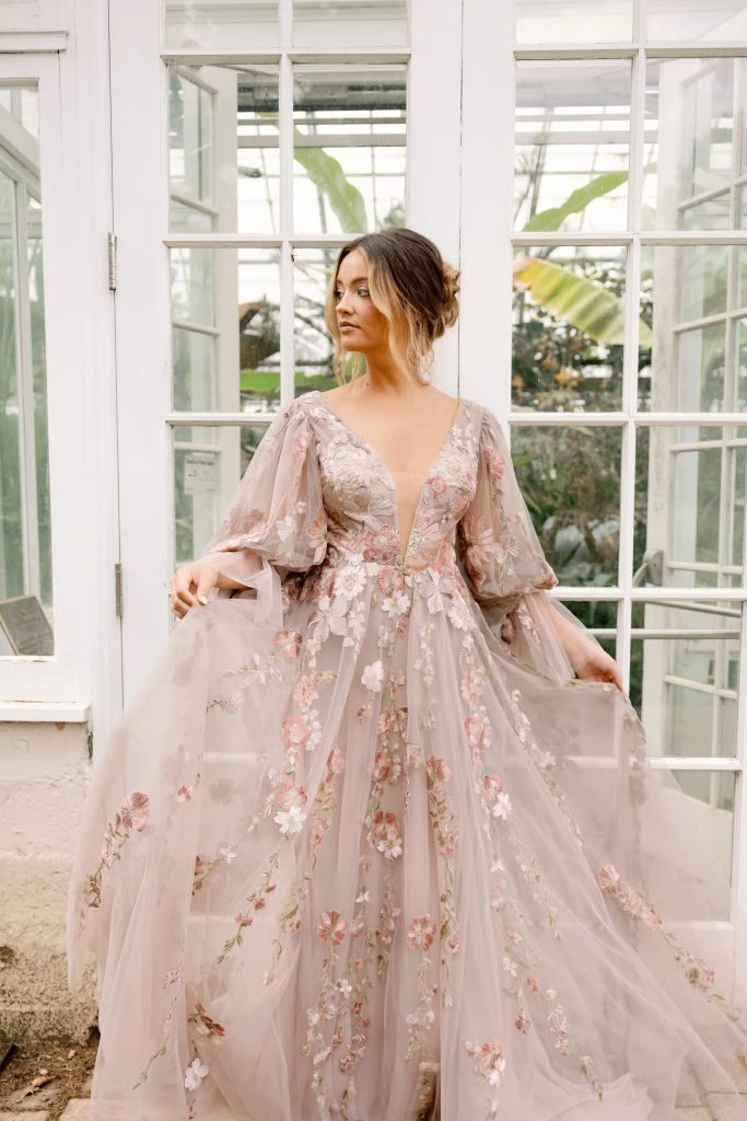 Bride wearing a long sleeve blush floral wedding dress in front of two french doors.