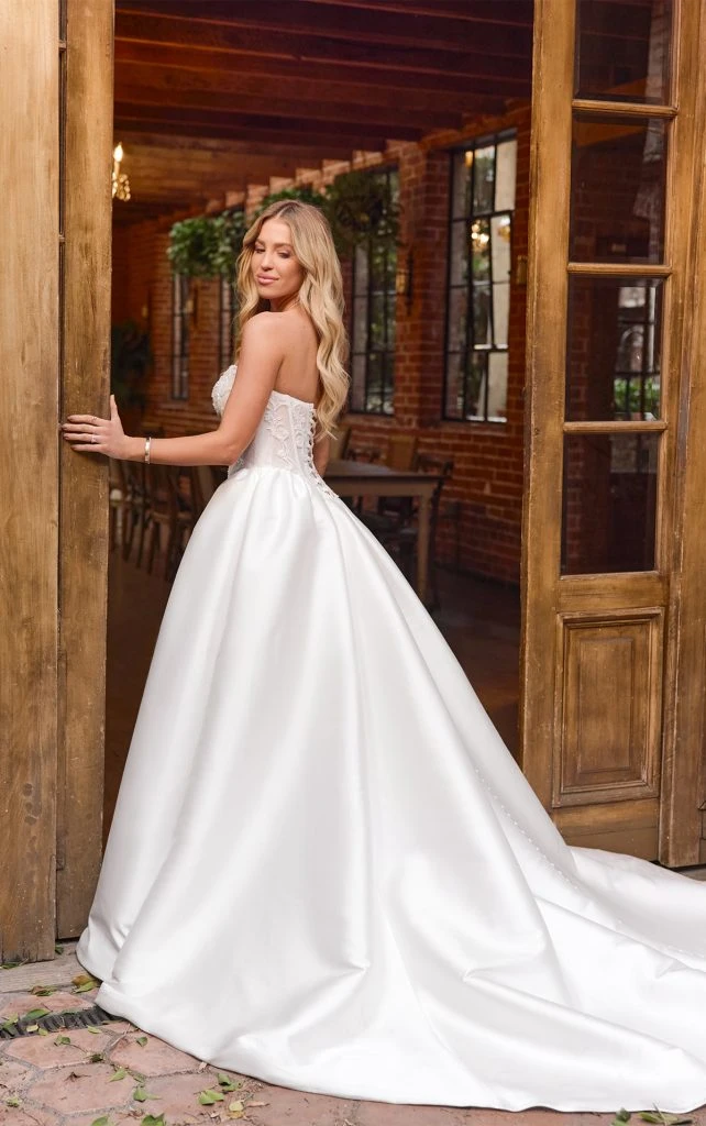 Bride wearing strapless ballgown wedding dress with lace up back detail standing in doorway
