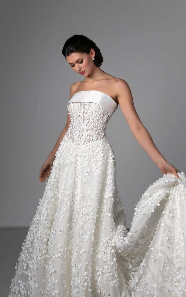 Bride wearing strapless romantic wedding dress with 3D floral and pearl details holding the train