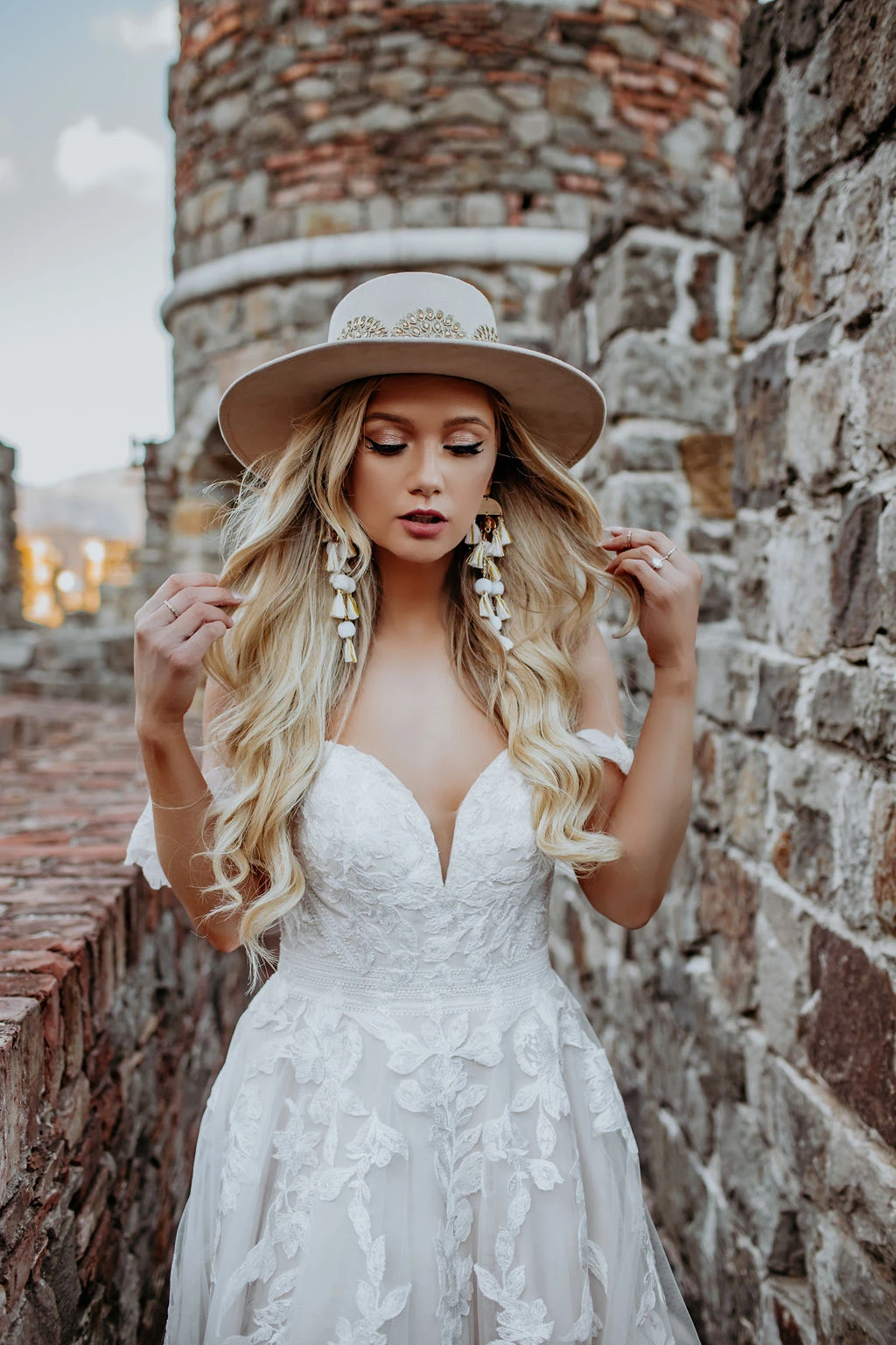 blonde bride wearing wide brim hat and long earrings and Stella York style 7332