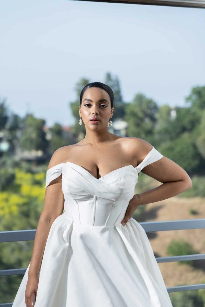 Plus size bride wearing off-the-shoulder ballgown wedding dress with exposed boning and ruched sweetheart neckline