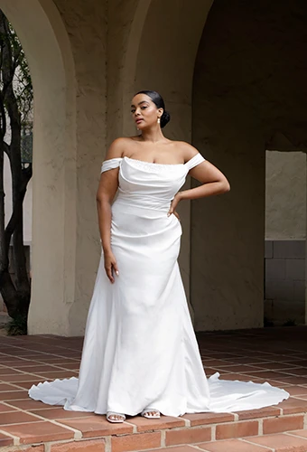 Plus-size bride wearing fit-and-flare wedding dress with off-the-shoulder straps and pearl details