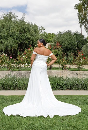 Plus-size bride wearing off-the-shoulder wedding dress with a circle train and fabric-covered buttons.