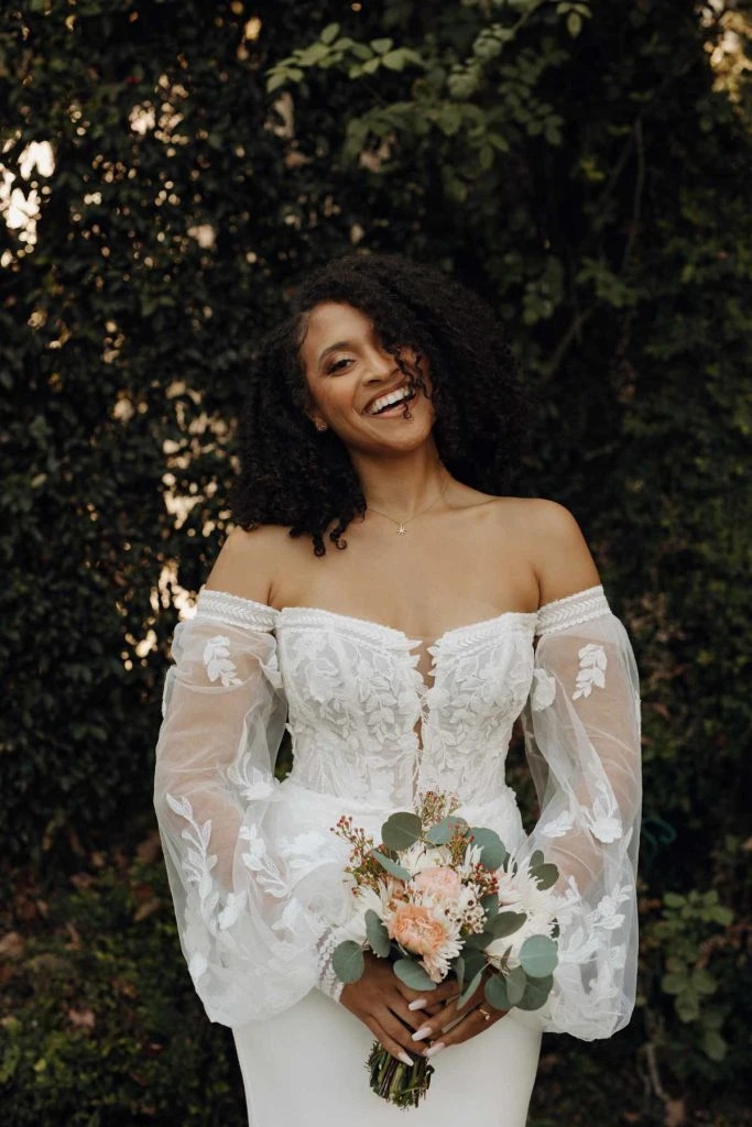 Bride wearing sheath wedding dress with long blouson sleeves, lace details and v-neckline.