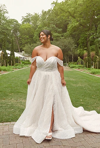 Plus-size bride wearing off-the-shoulder wedding dress with high leg slit in garden