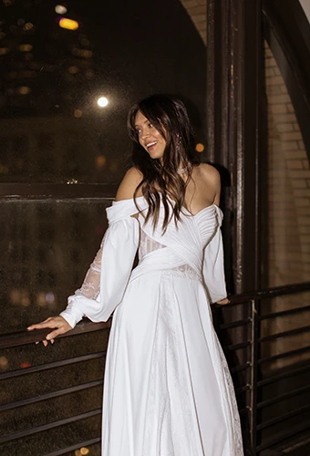bride leaning against iron railing wearing boho long sleeve wedding dress - dune by all who wander