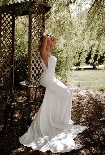 bride posing against garden bench wearing simple sheath wedding dress - jules by all who wander