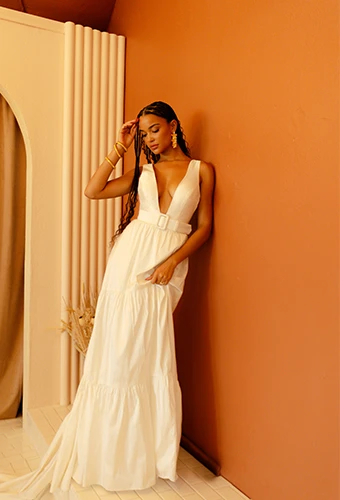 bride lenaing against orange wall in wedding dress with thick belt - kenedy by All Who Wander