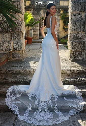 Bride wearing sheath wedding dress with fabric covered buttons and floral lace on stairs