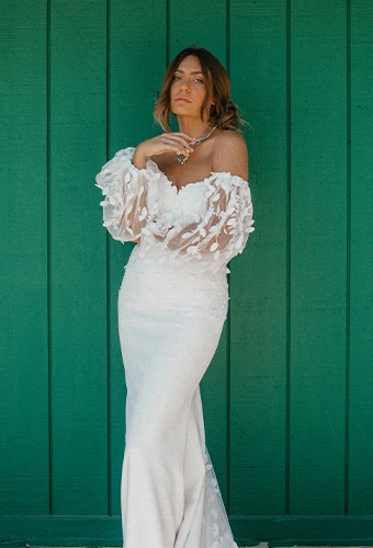 Bride wearing floral lace fit-and-flare wedding dress with blouson sleeves standing in front of green wall