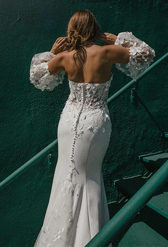 Bride wearing floral lace fit-and-flare wedding dress with blouson sleeves and fabric-covered buttons on green staircase