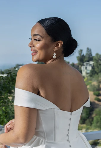Plus size bride wearing wedding dress with off the shoulder straps and statement earrings with a sleek bun