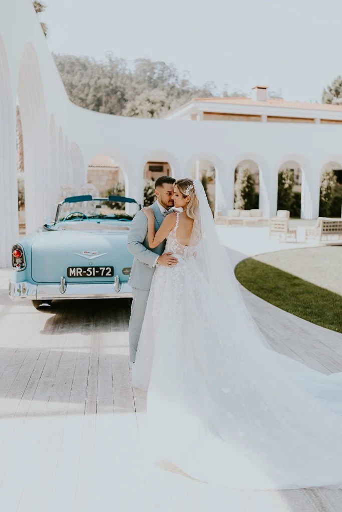 True bride Claudia posing with her husband in front of vintage car