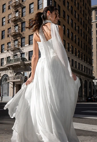 Bride wearing simple strapless wedding dress walking across a city street