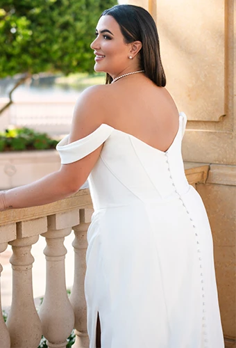 Plus size bride wearing simple wedding dress with off-the-shoulder straps and fabric covered buttons down the back