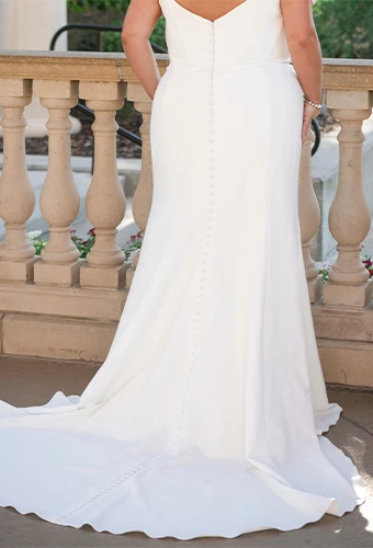 Plus size bride wearing simple wedding dress with off-the-shoulder straps and fabric covered buttons down the back