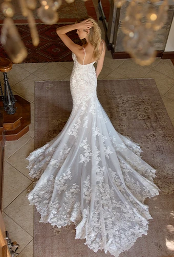 Bride wearing lace fit-and-flare wedding dress with long train and spaghetti straps 