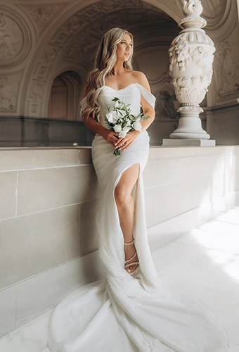 Petite bride wearing sparkling off-the-shoulder wedding dress with high leg slit