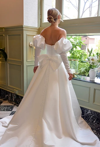 Brid wearing strapless wedding dress with detachable overskirt, bow back detail and puff sleeves