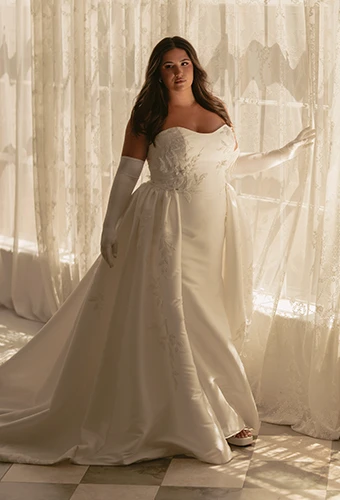 Plus size bride wearing fit-and-flare wedding dress with overskirt, sweetheart neckline and lace details