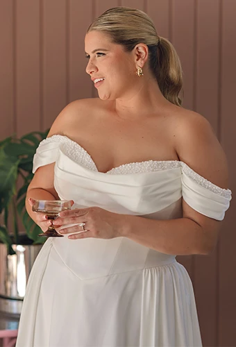 Plus size bride wearing satin wedding dress with off the shoulder straps and pearl neckline
