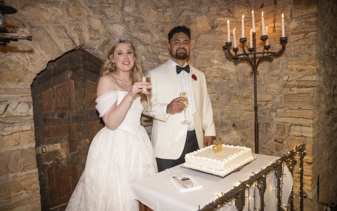 True bride Jaimee posing with her husband with their wedding cake