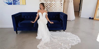 bride sitting on a blue velvet couch in an off the shoulder sheath wedding gown