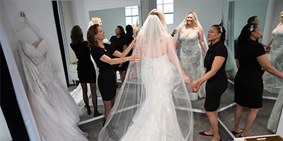 plus size bride standing in front of a mirror with stylist in a veil and mermaid wedding dress