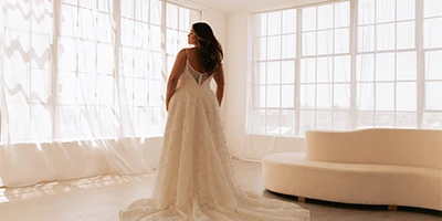 plus size bride posing in front of a sunny room in a lace open back ballgown