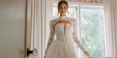 bride standing in front of window in a lace a-line wedding dress with detachable bolero