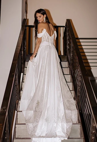 Bride wearing lace and chiffon wedding dress with draped sleeves on staircase