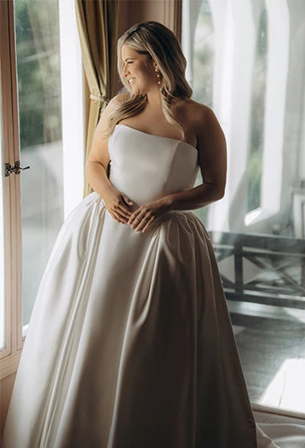 Plus size bride wearing strapless mikado A-line wedding dress with structured bodice, architectural seaming, and hidden pockets