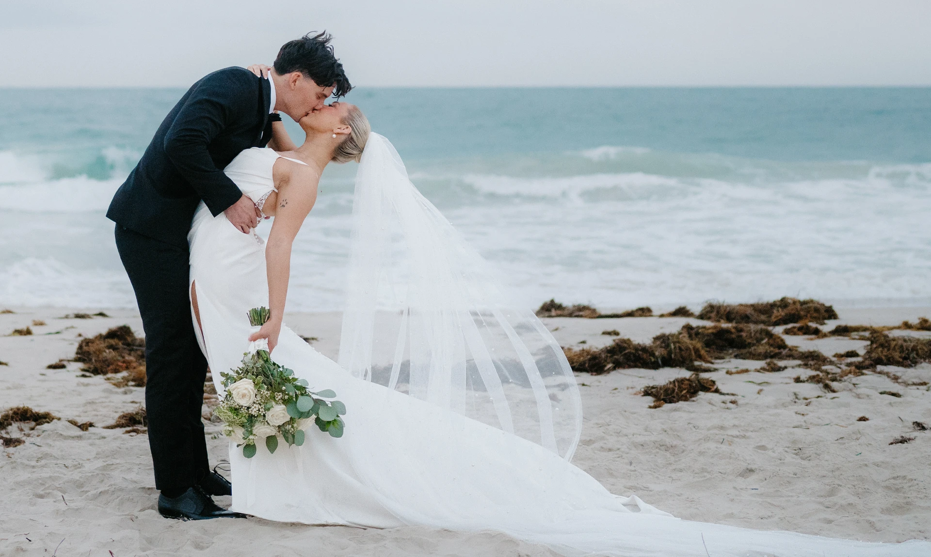 couple kissing on the beach in wedding dress and suit