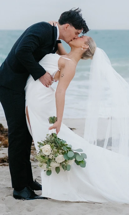 man dipping and kissing his bride on the beach