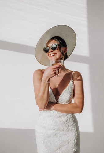 Bride wearing ML1305, a 3D lace wedding gown with a v-neck, featuring a statement hat and bridal sunglasses