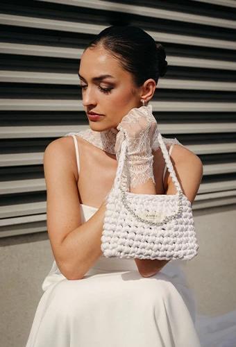 Bride wearing AWW jules, a spaghetti strap wedding dress with side cutouts, featuring a clutch bag