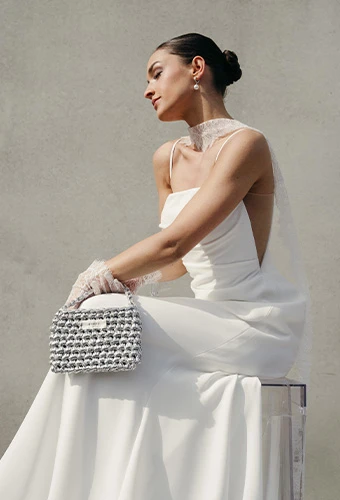 Bride wearing AWW jules, a spaghetti strap column wedding dress with side cutouts, featuring a clutch bag