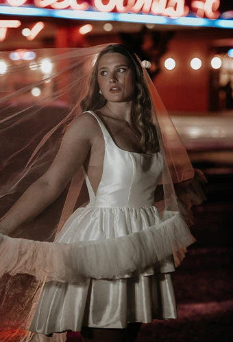 Bride wearing AWW london, a satin short a-line wedding dress with underskirt, paired with a blusher veil