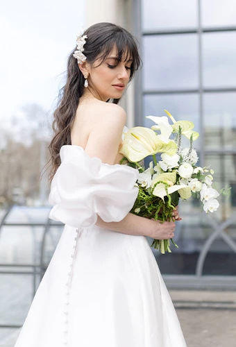 Bride wearing simple wedding gown with puff sleeves and holding a bouquet