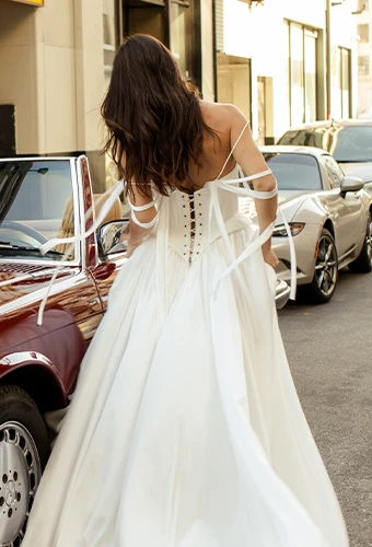 Bride wearing simple a line wedding gown with off the shoulder straps and ribbons