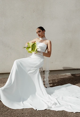 Bride wearing simple wedding gown posing in chair with bouquet