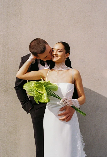 Bride waring simple wedding gown with thin spaghetti straps posing with her husban
