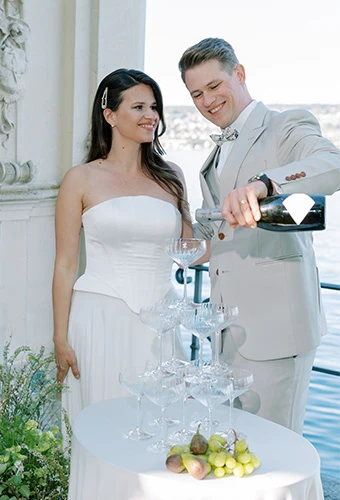 Bride wearing simple strapless wedding gown pouring champagne with her husband
